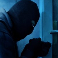 Masked thief using lock picker to open locked door