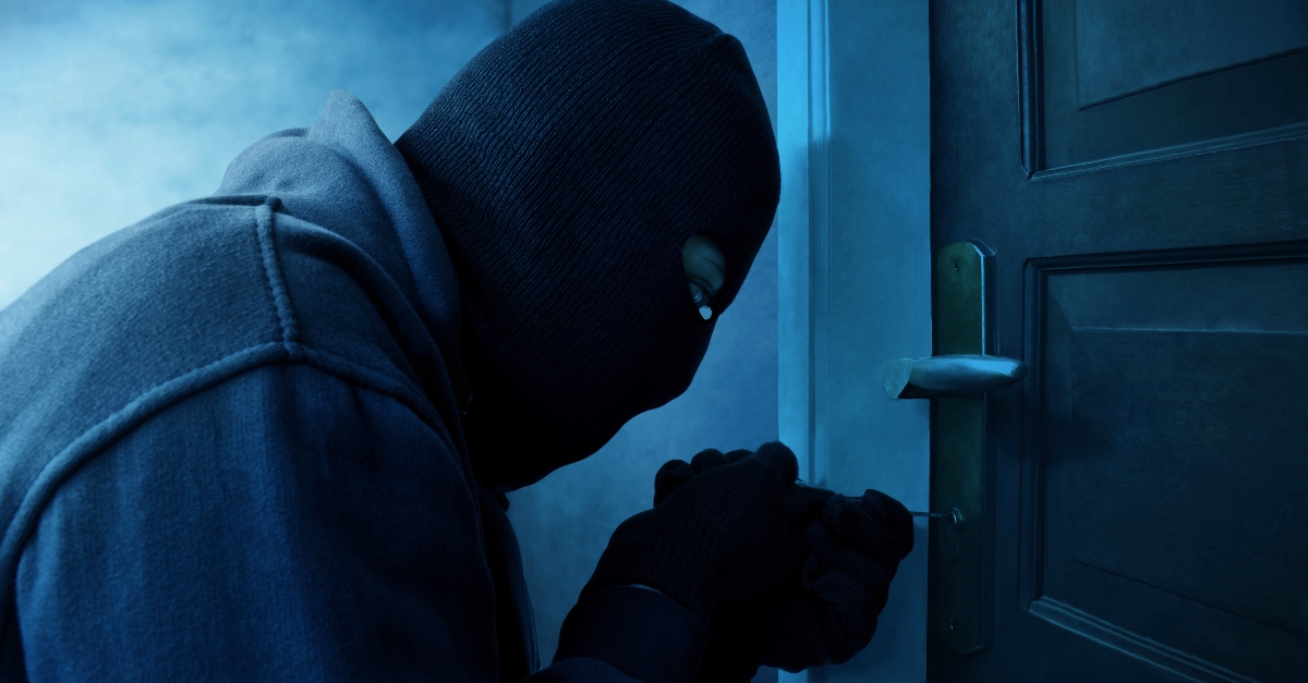 Masked thief using lock picker to open locked door